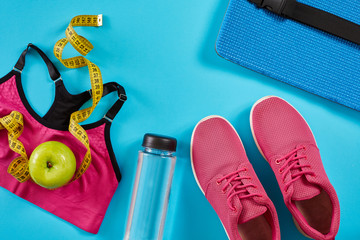 Sneakers with measuring tape on cyan blue background. Centimeter in yellow color, pink sneakers, female sport top and bottle of water, copy space.