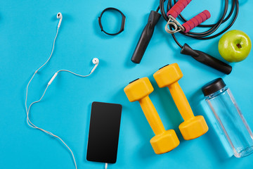 Dumbbells, mobile phone and skipping rope on blue background. Top view. Fitness, sport and healthy lifestyle concept.