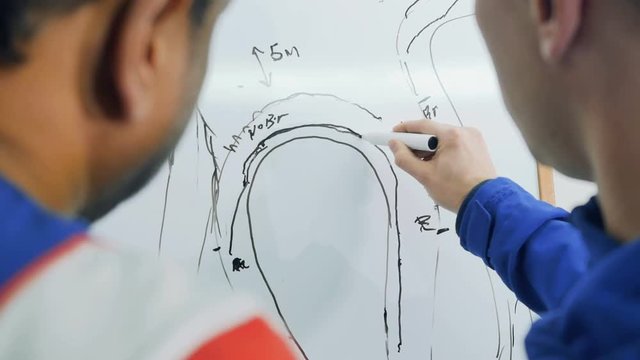 Two sportsmen draws the plan of car racing at flipchart