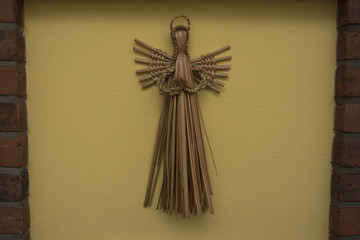 The handmade original czech cattail decoration of angel is hanging on the yellow wall.