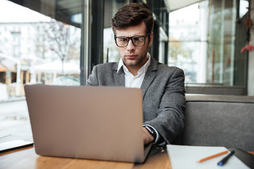 Concentrated business man in eyeglasses sitting by the table