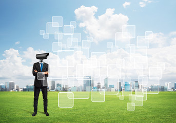 Camera headed man standing on green grass against modern cityscape