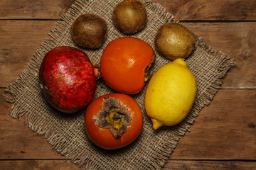 Persimmon, kiwi, pomegranate on a platter on a wooden table.
