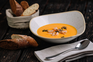 Pumpkin shrimp cream soup served with bread and spoon on dark wood background