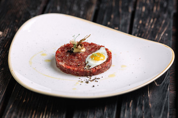 Beef tartare with fried quail egg on dark wood background