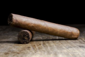 Two Cuban cigars lying on an old wooden table