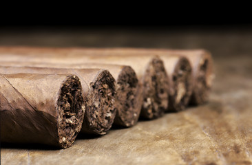 Row of six Cuban cigars lying on an old wooden table