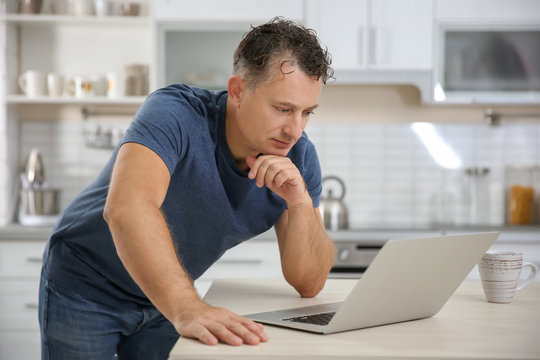Handsome mature man using laptop in kitchen