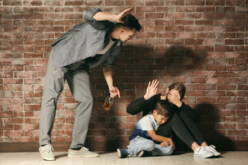 Fototapeta na wymiar Drunk man threatening his wife and son against brick wall