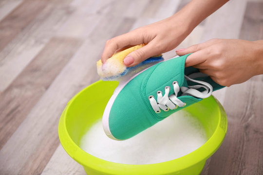 Woman washing sneaker with sponge over plastic basin, closeup