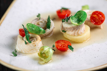 Rolled herring with vegetable on irregular shape plate on dark wood background