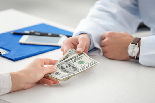 Woman giving money to doctor in office, closeup