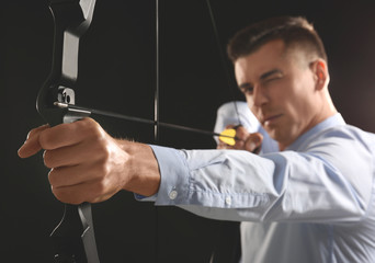 Young businessman practicing archery on dark background