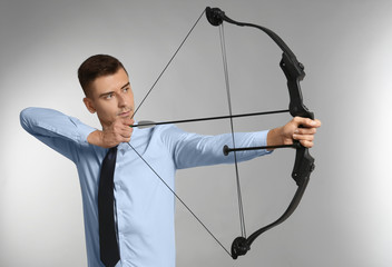 Young businessman practicing archery on grey background