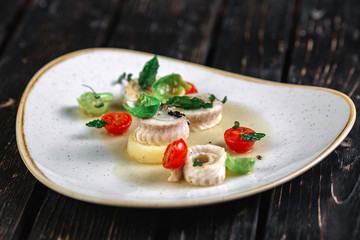 Rolled herring with vegetable on irregular shape plate on dark wood background