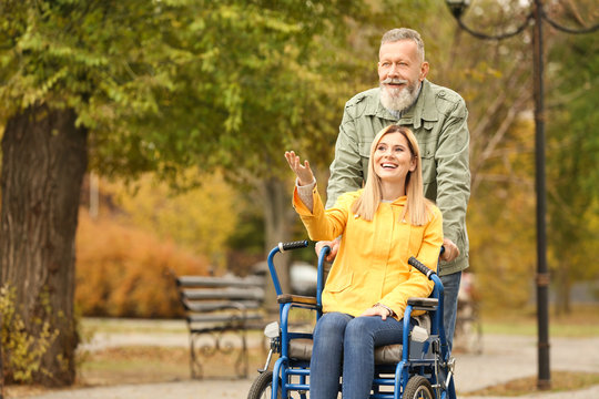 Senior man with his daughter in wheelchair outdoors on autumn day
