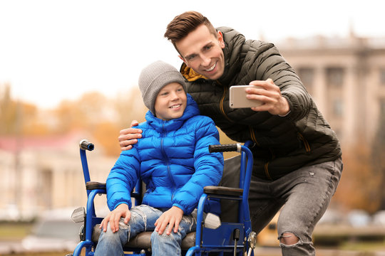 Man with his son in wheelchair taking selfie outdoors on autumn day