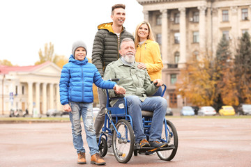 Elderly man in wheelchair with his family outdoors on autumn day