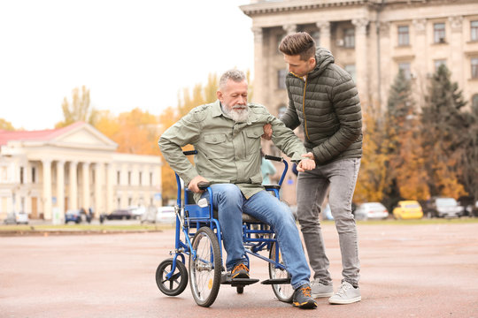 Man helping his elderly father to get up from wheelchair outdoors