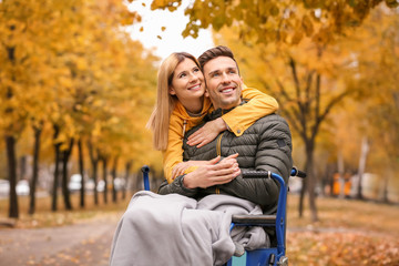 Woman with her husband in wheelchair outdoors on autumn day