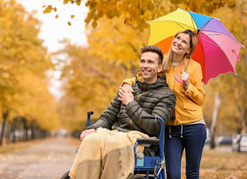 Woman with her husband in wheelchair outdoors on autumn day