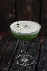 Green alcohol cocktail with foam on the dark wood background