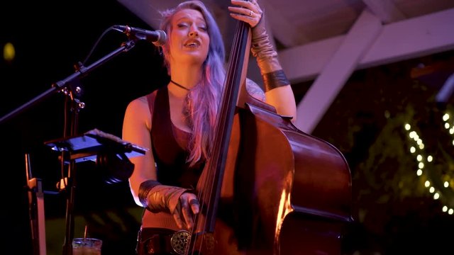 Closeup of female stand-up or double bass player with pierces and tattoos under blue lights.