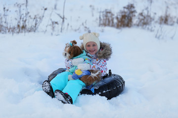 Winter portrait of a girl with a puppy on a tubing. A girl and a dog ride on a hill in the winter.