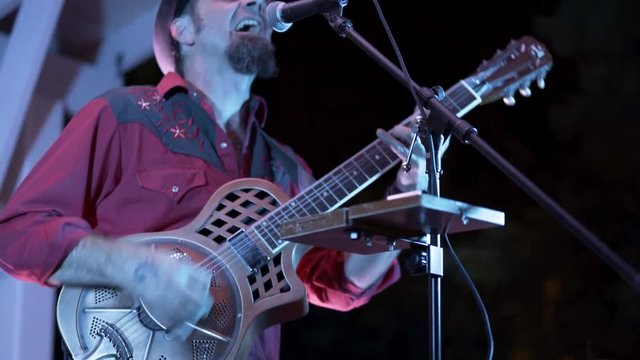 Closeup of guitarist playing a resonator at a live performance outside at night.