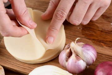 Cooking techniques. Closeup of woman hands making dumplings on wooden board