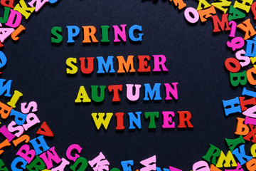 concept design - the word SPRING SUMMER AUTUMN WINTER from multi-colored wooden letters on a black background, creative idea