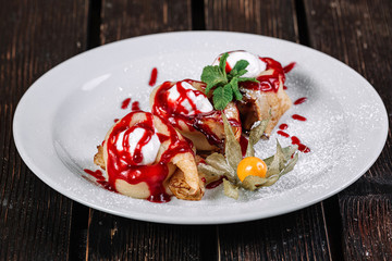 Pancakes with sour cream and jam on white plate on dark wood background.