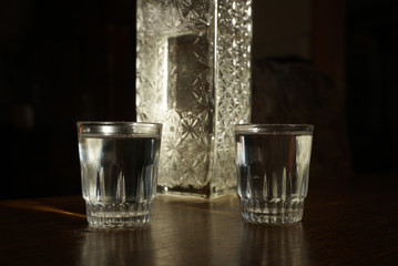 two glasses of vodka and a bottle stand on a table on a dark background