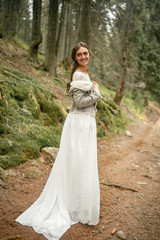 Bride stands on forest road, smiles and looks back.