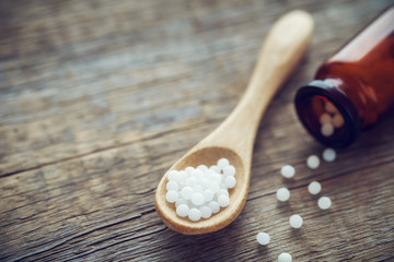 Wooden spoon of homeopathic globules, bottle and scattered granules. Homeopathy medicine.