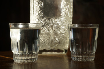 two glasses of vodka and a bottle stand on a table on a dark background