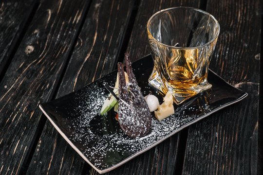 Whiskey and appetizer on black plate on dark wood background