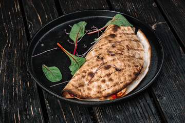 Pita wrapped with meat on the frying pan on dark wood background
