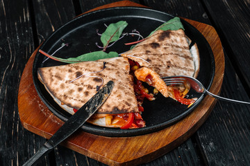 Pita wrapped with meat served with knife and fork on the frying pan on dark wood background