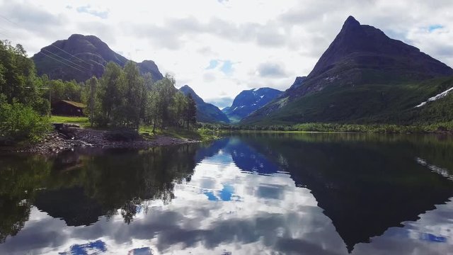 Drone flying through Norways most beautiful mountain valley. Lake reflecting the surreal landscape. Establishing intro shot.