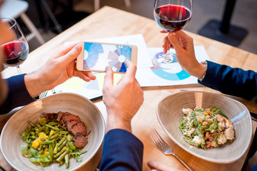 Business couple having a conversation with charts and graphs during the dinner with wine and meals at the restaurant