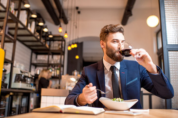 Elegant businessman dressed in the suit having a dinner with salad and wine sitting at the modern restaurant interior