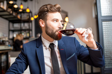 Handsome businessman dressed in the suit drinking red wine sitting at the restaurant