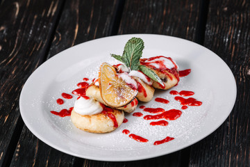 Сottage pancake with sour cream and jam on white plate on dark wood background.