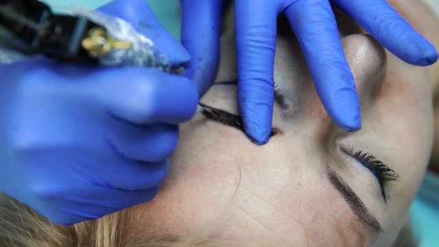 Permanent Makeup For Eyebrows. Closeup Of Beautiful Woman With Thick Browser In Beauty Salon. Beautician Doing Eyebrow Tattooing For Female Face. Beauty Procedure.