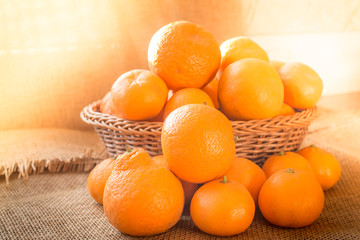 Fresh ripe fruit tangerine oranges in a basket with rustic background and with morning sunlight effect.