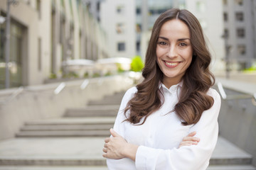 Portrait of a confident modern business woman with beautiful lush hair on the background of an office center in the city and looks on camera.