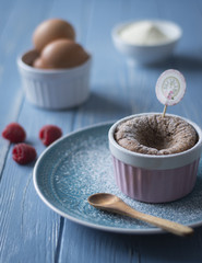 Schokoladensouffle in rosa Keramikförmchen auf blauem Teller mit frischen Früchten 