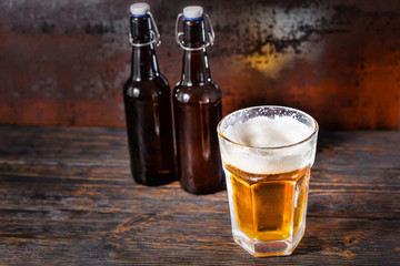 Two beer bottles near glass with a light beer and a head of foam on old dark desk