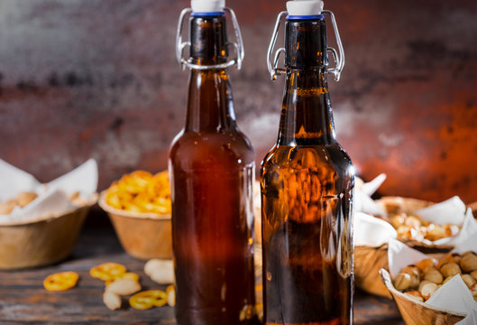 Two beer bottles, plates with pistachios, small pretzels and peanuts on background